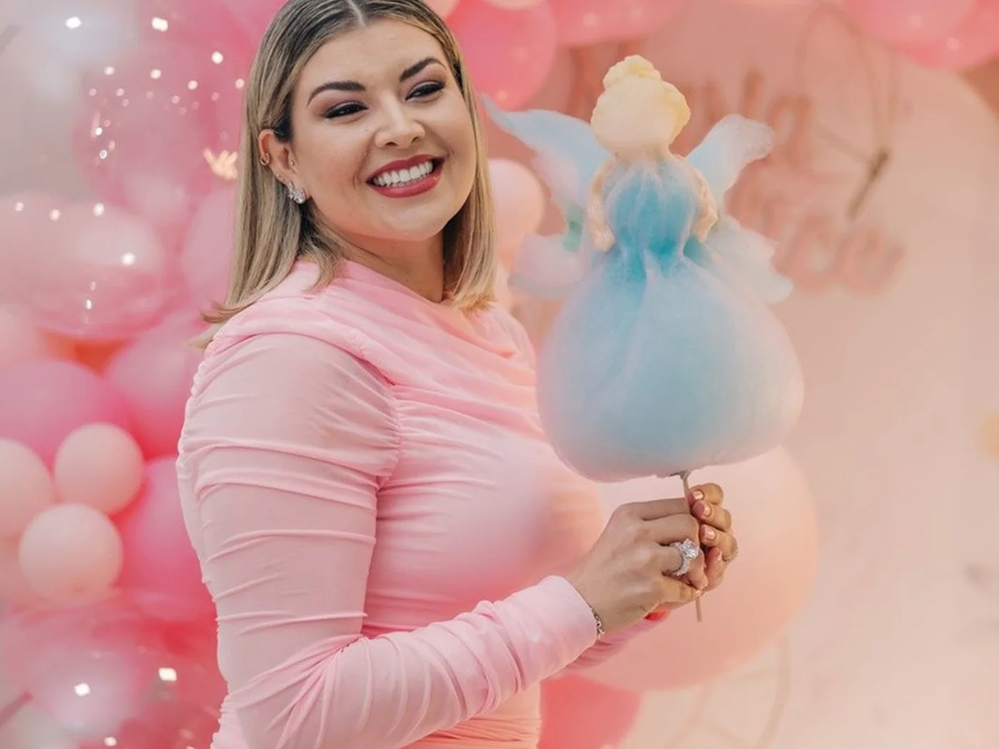 Convidada segurando escultura de algodão doce em formato de personagem, em festa com decoração rosa
